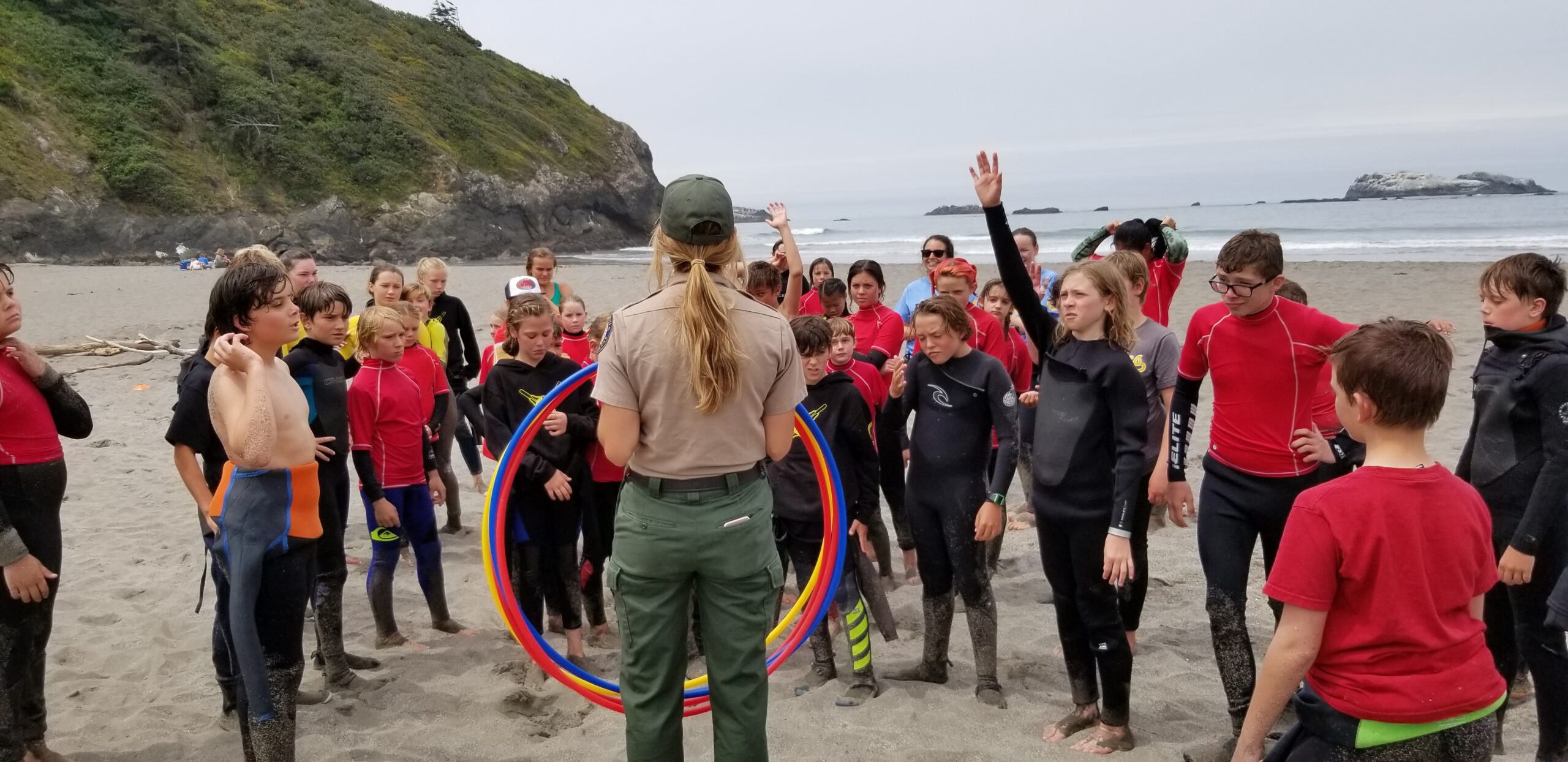 Group of hikers in a forest observing a man examining ferns and mushrooms along the trail.
