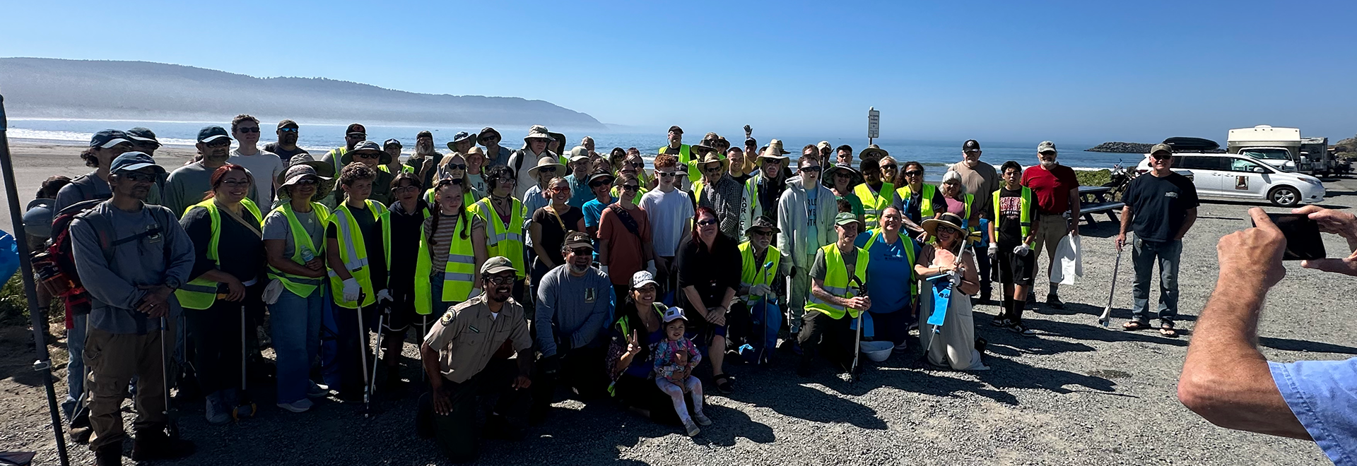 A group of people gather at night under a starry sky near a tall lookout tower, participating in a volunteer event at a park, marveling at the celestial wonders above.
